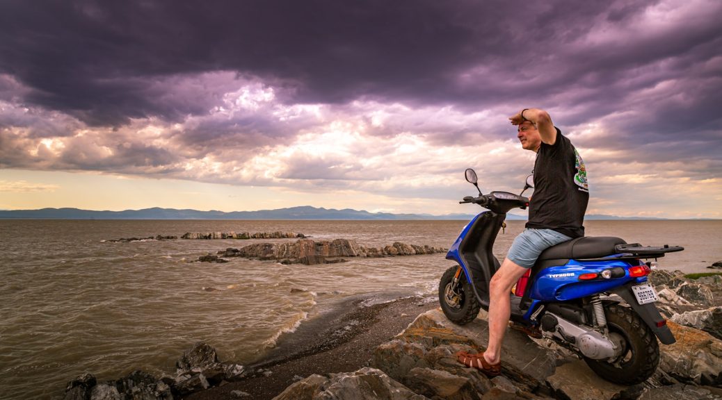man in black jacket and blue denim jeans sitting on motorcycle on shore during daytime