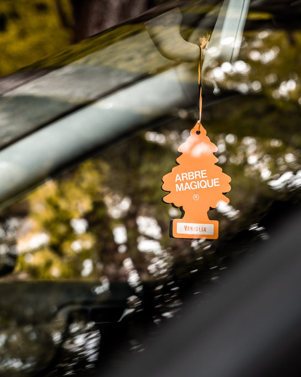 From above through glass view of ornamental orange cardboard in form of tree hanging on golden braid inside of automobile with glowing surface