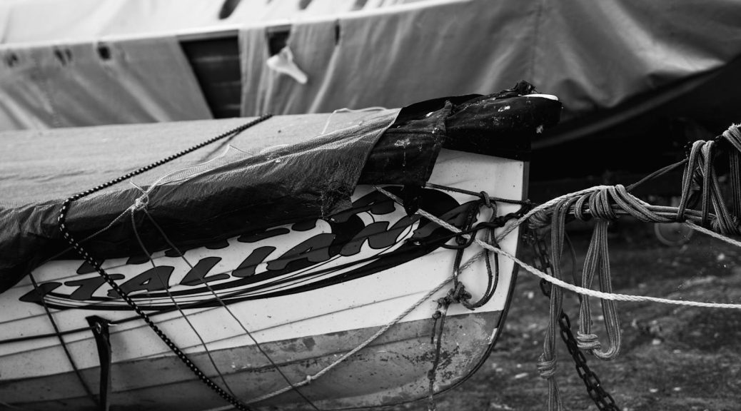 Detailed black and white image of an old boat covered with tarps on a beach, showcasing textures.
