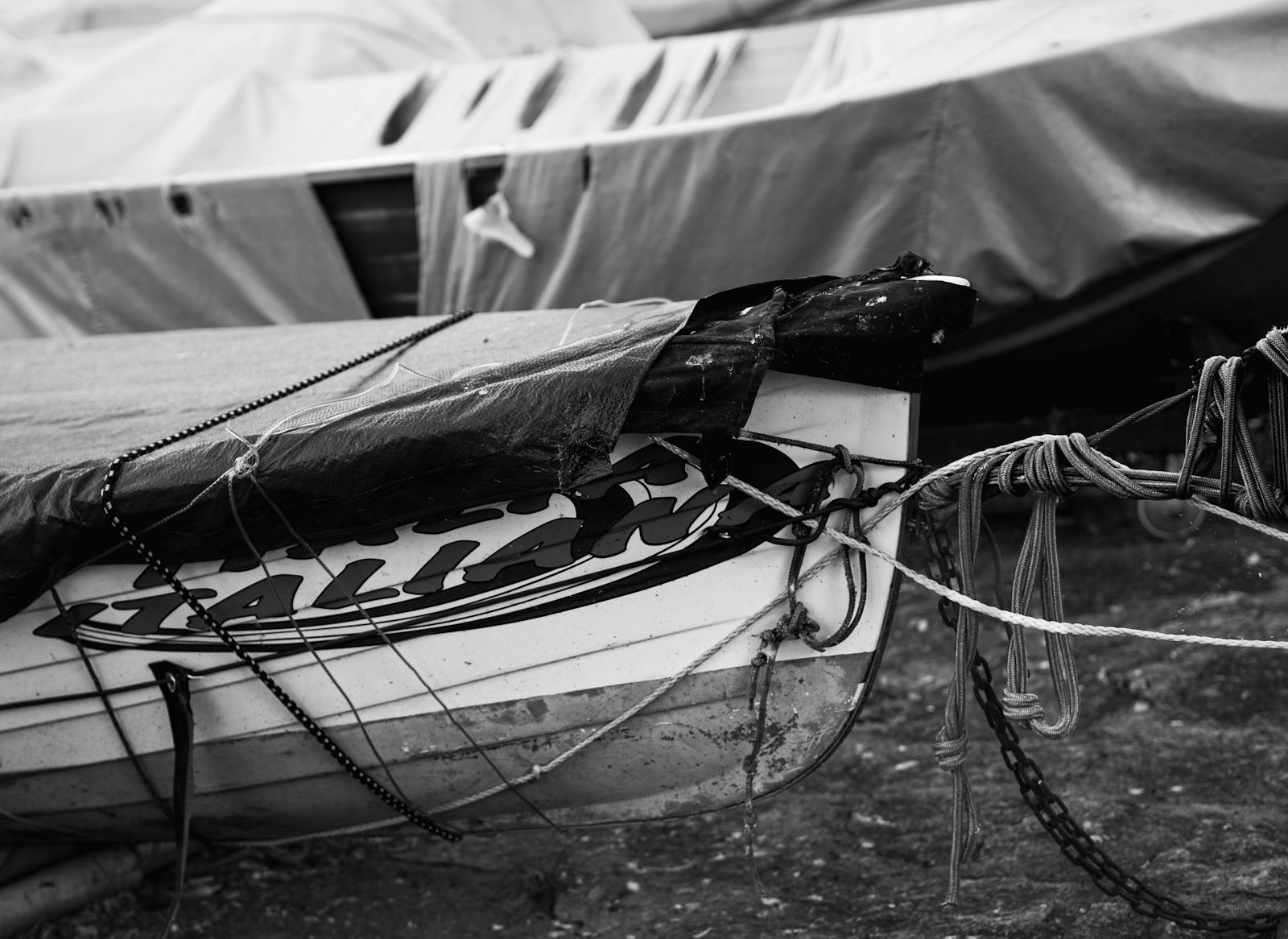 Detailed black and white image of an old boat covered with tarps on a beach, showcasing textures.